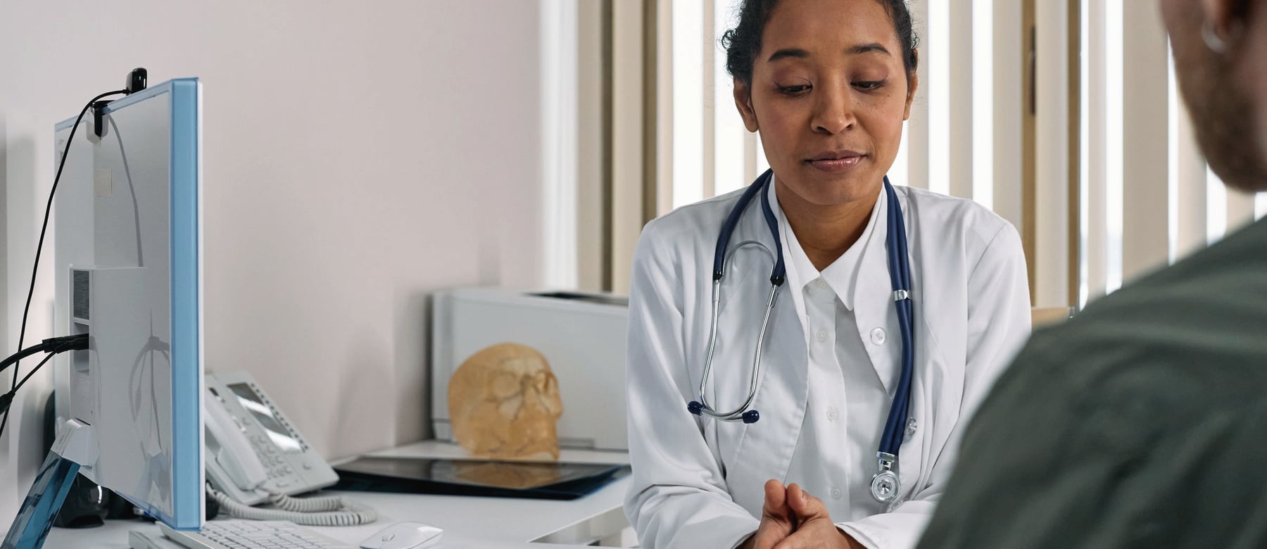 A clinician listening to a patient across a consulting-room desk.