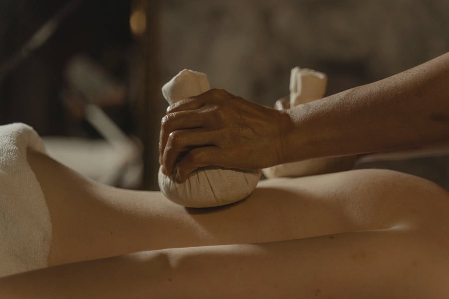 A therapist applying warm herbal poultices to a person's back during an Ayurvedic treatment.