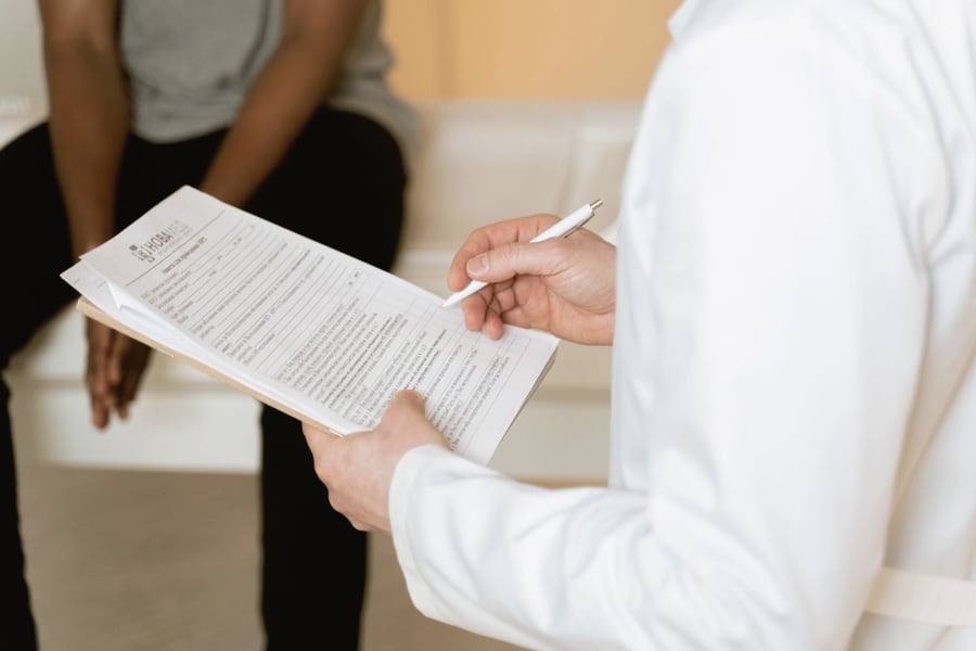 A clinician in a white coat reviewing a patient's assessment notes during a consultation.