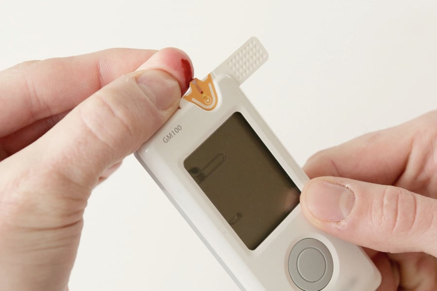 A blood glucose reading being taken with a handheld monitor.